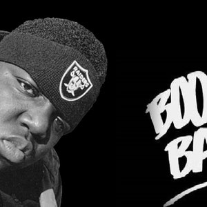 Könnte beinhalten: Schwarzweißfoto eines Mannes mit einer schwarzen Mütze mit einem weißen Raiders-Logo. Der Text "BOOM BAP!" ist in Weiß auf schwarzem Hintergrund geschrieben.