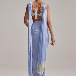 May include: A light blue formal gown with a draped shawl and pearl accents. The backless bodice is embellished with intricate lace and a pearl necklace. The shawl features pearl fringe.