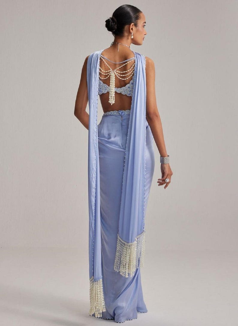 May include: A light blue formal gown with a draped shawl and pearl accents. The backless bodice is embellished with intricate lace and a pearl necklace. The shawl features pearl fringe.