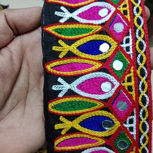 May include: Black fabric trim with colorful embroidery and small round mirrors. The trim features a repeating pattern of fish shapes, geometric designs, and a border of small circles.