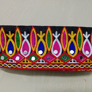 Puede incluir: Borde de tela negra con bordado colorido y pequeños espejos redondos. El borde presenta un patrón repetitivo de formas de lágrima con hilo amarillo, rosa, azul, verde y blanco.