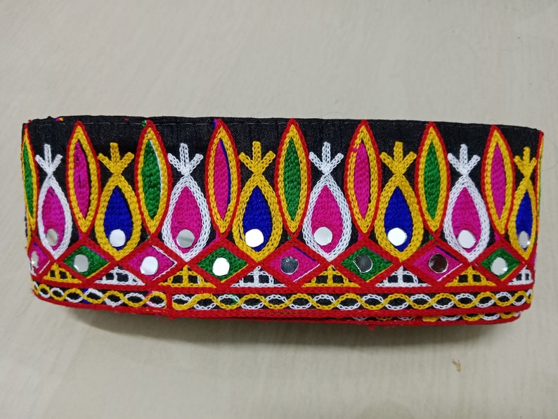 May include: Black fabric trim with colorful embroidery and small round mirrors. The trim features a repeating pattern of teardrop shapes with yellow, pink, blue, green, and white thread.