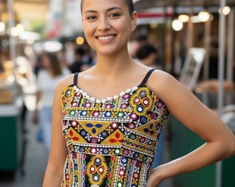 May include: A sleeveless top featuring intricate multi-colored embroidery in yellow, red, blue, and green thread. The garment is adorned with small circular mirrors, decorative white beads along the neckline, and a scalloped hem with white fringe.