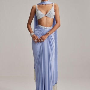 May include: A light blue formal outfit featuring a beaded crop top, matching draped skirt, and a scarf. The outfit includes a beaded belt and a draped scarf with a beaded fringe. The ensemble is suitable for special occasions.