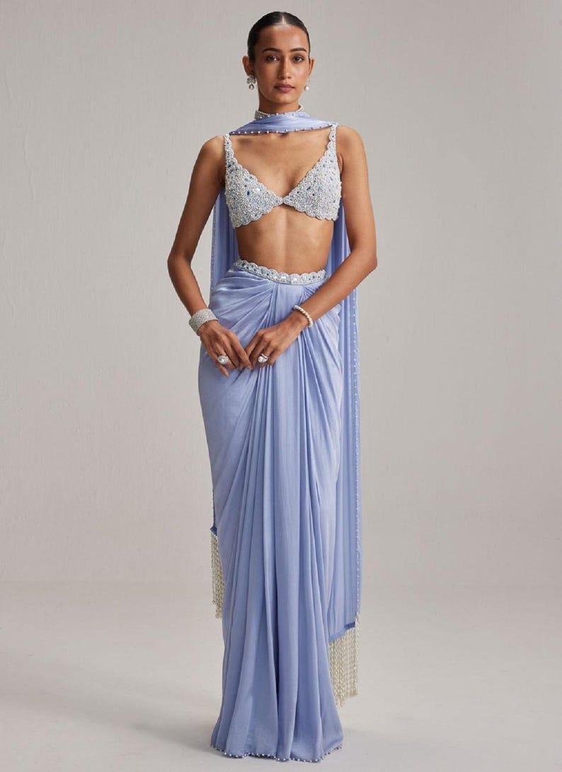 May include: A light blue formal outfit featuring a beaded crop top, matching draped skirt, and a scarf. The outfit includes a beaded belt and a draped scarf with a beaded fringe. The ensemble is suitable for special occasions.