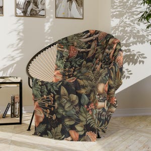 May include: A throw blanket with a dark green background and a pattern of mushrooms, leaves, and ferns. The blanket is draped over a chair.