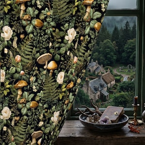 Könnte beinhalten: Ein dunkler Vorhang mit einem botanischen Muster aus Pilzen, Farnen und Rosen. Der Vorhang ist teilweise geöffnet und gibt den Blick auf ein Dorf in einem Tal frei. Auf einem Holztisch stehen eine Schale mit Kristallen, ein Buch und andere dekorative Gegenstände.