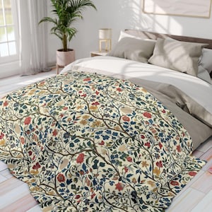 Puede incluir: Una manta con estampado floral sobre un fondo crema, con un diseño de ramas entrelazadas, flores rojas, azules y amarillas. La manta está sobre una cama con ropa de cama de colores neutros, creando un ambiente acogedor.