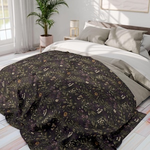 May include: A dark floral patterned blanket on a bed. The blanket displays a repeating pattern of small flowers and foliage in white, yellow, and purple against a dark background. The bed has white and grey bedding.