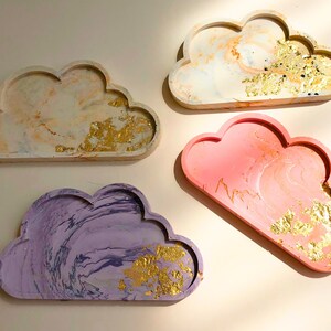 May include: Four cloud-shaped trays with gold accents. The trays are made of a marbled material and come in four colours: white, pink, purple, and light brown.