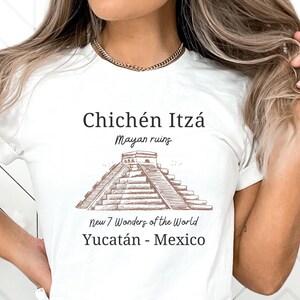May include: White t-shirt with a brown line drawing of the Chichén Itzá Mayan ruins in Mexico. The text "Chichén Itzá Mayan ruins New 7 Wonders of the World Yucatán - Mexico" is printed on the shirt.