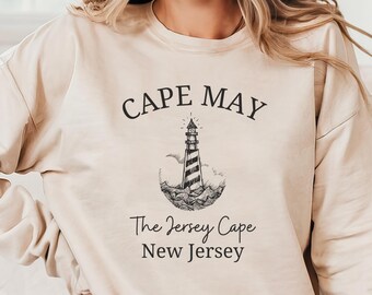 May include: A beige sweatshirt with a black graphic design of a lighthouse and the text "CAPE MAY The Jersey Cape New Jersey".