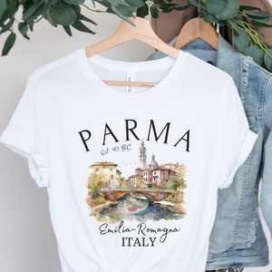 May include: White t-shirt with a black graphic design of the city of Parma, Italy. The graphic includes the text "PARMA Est. 183 BC" and a watercolor illustration of a bridge and buildings. The text "Emilia-Romagna ITALY" is also included in the design.