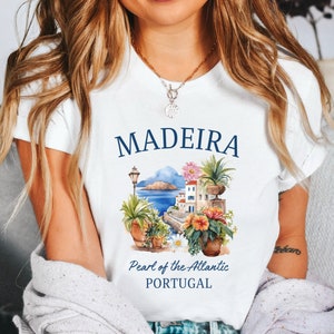 May include: White t-shirt with a graphic design of a cityscape with the text "MADEIRA Pearl of the Atlantic PORTUGAL".