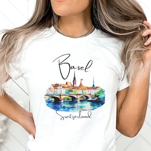 May include: White t-shirt with a watercolor illustration of the Basel cityscape, including a bridge and buildings. The text "Basel" and "Switzerland" are printed in black below the illustration.