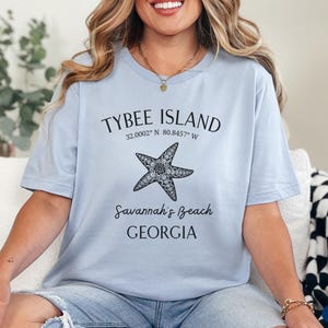 May include: A light blue t-shirt with a black graphic design featuring a starfish and the text "Tybee Island 32.0002&deg; N 80.8457&deg; W Savannah's Beach GEORGIA".