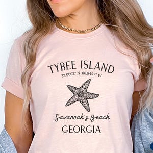 May include: A pink t-shirt with a black graphic design featuring a starfish and the text "Tybee Island 32.0002&deg; N 80.8457&deg; W Savannah's Beach GEORGIA".
