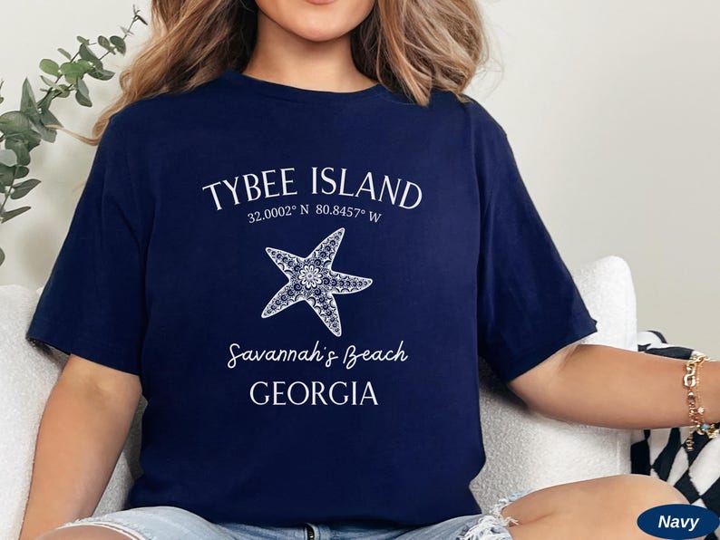 May include: Navy blue t-shirt with white text that reads "Tybee Island 32.0002&deg; N 80.8457&deg; W Savannah's Beach GEORGIA" and a white starfish graphic.