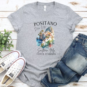 May include: A gray t-shirt with a watercolor illustration of Positano, Italy. The text on the shirt reads "Positano Dolce Vita Southern Italy Costa d'Amalfi".