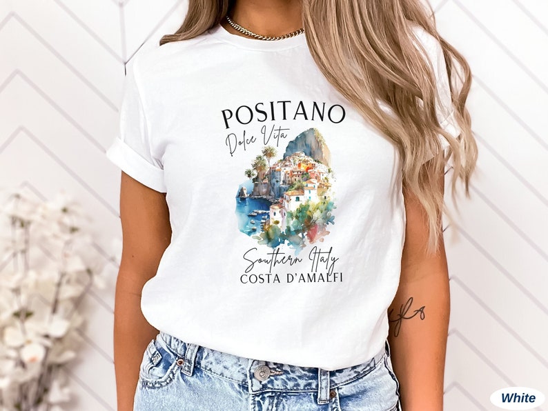 May include: White t-shirt with a watercolor illustration of Positano, Italy. The text "Positano Dolce Vita Southern Italy Costa D'Amalfi" is printed on the shirt.