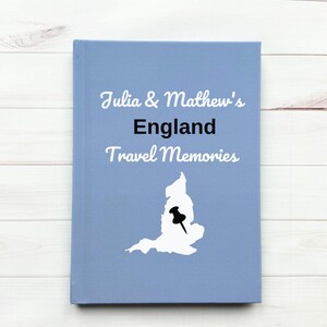 May include: A blue travel journal with the text "Julia & Matthew's England Travel Memories" and a white outline of England with a black pushpin in the center.