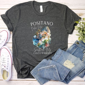 May include: Dark grey heather t-shirt with a watercolor illustration of Positano, Italy. The text "Positano, Dolce Vita, Southern Italy, Costa d'Amalfi" is printed on the shirt.