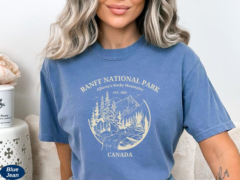 May include: A light blue t-shirt with a graphic print of a mountain scene and the text "Banff National Park, Alberta's Rocky Mountains, Est. 1885, Canada".