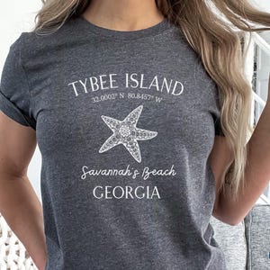 May include: Dark grey heather t-shirt with white text that reads "Tybee Island 32.0002&deg; N 80.8457&deg; W Savannah's Beach GEORGIA" and a white starfish graphic.
