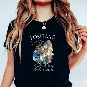 May include: Black t-shirt with a white graphic design featuring the text "Positano Dolce Vita" and a watercolor illustration of the town of Positano, Italy. The text "Southern Italy Costa d'Amalfi" is also included in the design.