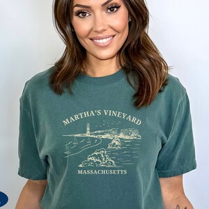 May include: A dark green t-shirt with a white graphic design of a lighthouse and the text "Martha's Vineyard, Massachusetts".
