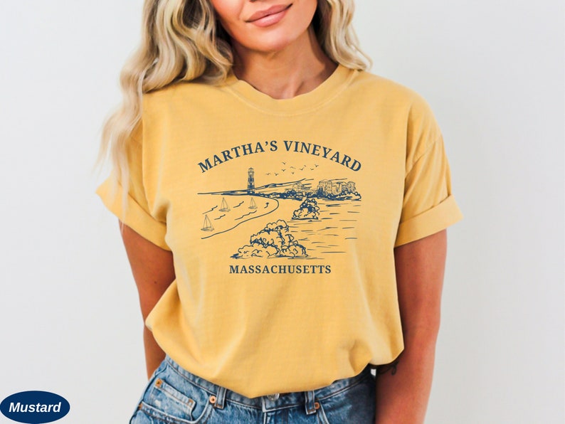 May include: A mustard yellow t-shirt with a graphic of a lighthouse, beach, and sailboats. The text "Martha's Vineyard, Massachusetts" is printed on the shirt.