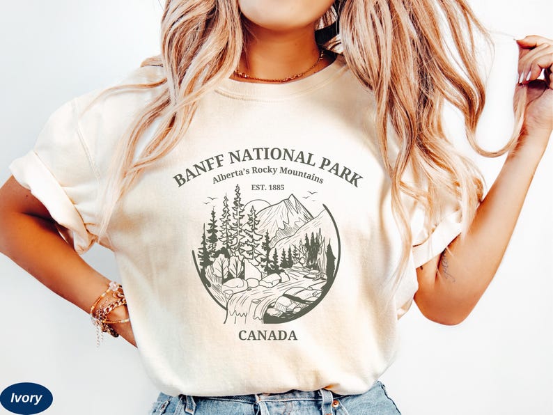 May include: A white t-shirt with a graphic design of a mountain scene with the text "Banff National Park, Alberta's Rocky Mountains, Est. 1885, Canada".
