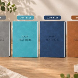May include: Four rectangular notebooks in grey, light blue, dark blue, and brown, each featuring a textured cover and the centred text YOUR TEXT HERE. The notebooks are arranged side-by-side, showcasing a consistent design with white page edges.