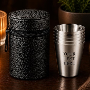 May include: A set of stainless steel shot glasses stacked together, featuring the engraved text "YOUR TEXT HERE" on the front, accompanied by a black, cylindrical, textured faux leather carrying case with a zip closure.