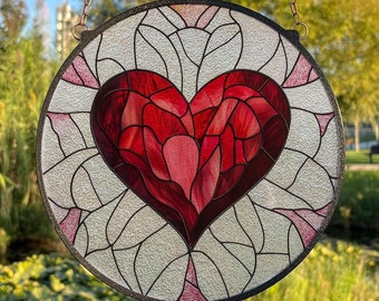 May include: A stained glass window hanging with a red heart design. The heart is made of many small pieces of glass and has a white background. The window is round and has a metal frame.