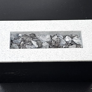 May include: A white rectangular fire pit with a black base. The fire pit has a rectangular opening filled with gray rocks.