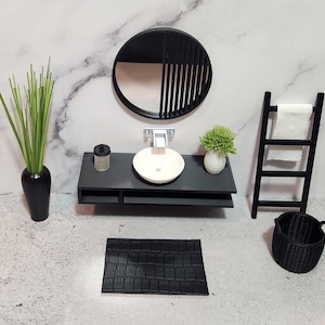 May include: Black and white bathroom vanity set with a round mirror, a white sink, a black towel rack, a black basket, and a black bath mat.