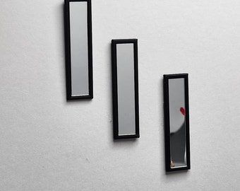 May include: Three black framed rectangular mirrors hanging on a white wall. The mirrors are all the same size and shape.