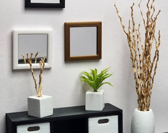 May include: A black shelf unit with three white storage bins. The shelf is decorated with three framed mirrors, a white vase with dried branches, and a white planter with a green plant.