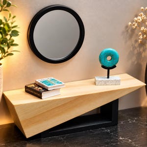 May include: A light-colored wooden shelf with an angled top surface and a black rectangular base. On the shelf sit two small books titled Leonardo da Vinci and Van Gogh, and a turquoise donut-shaped stone sculpture on a black and white stand.