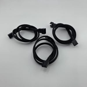 May include: Three black braided fan extension cables with black connectors. The cables are looped and arranged on a white surface. The connectors are rectangular with multiple pins.