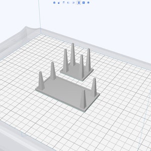 May include: Two gray 3D printed stands with four vertical supports each. The stands are designed to hold objects upright.