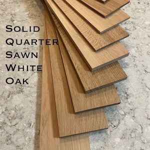 May include: Close-up of multiple pieces of solid quarter sawn white oak wood. The wood is light brown in color and has a natural grain pattern. The wood is arranged in a fan shape.