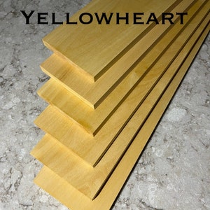 May include: Stack of five solid yellowheart wood boards. The boards are smooth and have a light yellow color. The text "SOLID YELLOWHEART" is printed on the top board.