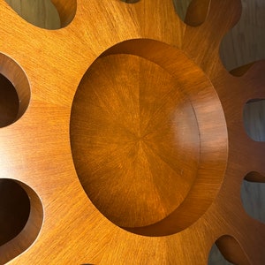 May include: A wooden sunburst wall decor with a circular cutout in the center. The wood is a rich brown color and has a smooth finish.