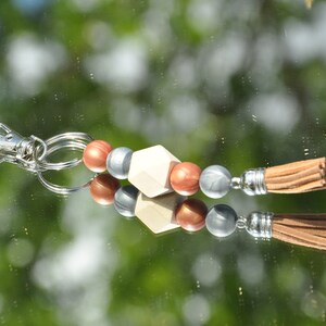 May include: A white wooden geometric bead keychain with silver and copper colored beads and a brown tassel.