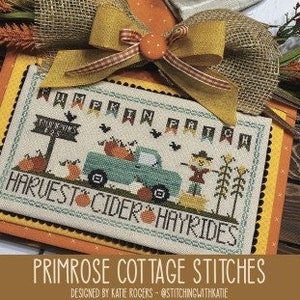 May include: Cross stitch pattern featuring a vintage truck with pumpkins, a scarecrow, and a sign that reads "Pumpkin Patch". The pattern is surrounded by a border of fall-colored banners that read "Pumpkin Patch". The pattern is titled "Harvest Cider Hayrides" and is designed by Katie Rogers.