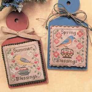 May include: Two wooden signs with cross-stitch embroidery. The blue sign says "Spring Blessings" with a bluebird and flowers. The red sign says "Summer Blessings" with a yellow bird and flowers.