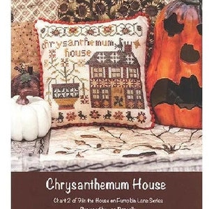 Puede incluir: Patrón de punto de cruz para una casa con una planta de crisantemo en frente. El patrón se titula "Chrysanthemum House" y es parte de una serie llamada "9 in the House on Fumo Lane". El patrón fue diseñado por Lor Pengelly.