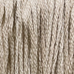 May include: Close-up of a skein of beige embroidery floss. The floss is made of 100% cotton and is perfect for hand embroidery projects. The skein is labeled "Mariner's Compass".